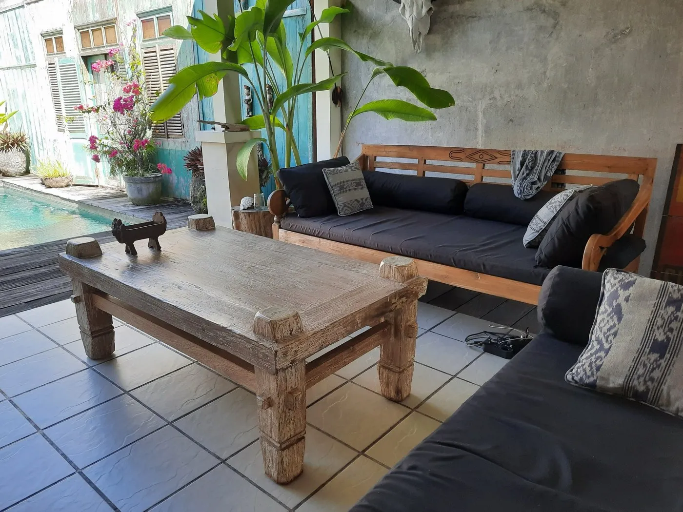 A poolside terrace with a reclaimed-teak daybed, low table and ikat cushions