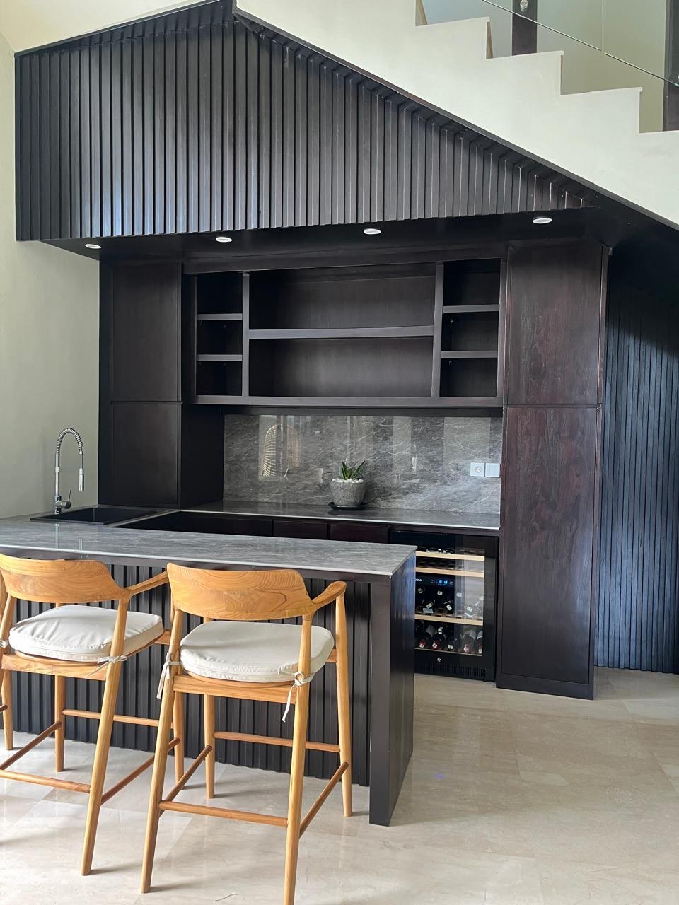 Fitted dark-stained timber joinery and a fluted bar counter built into an under-stair space