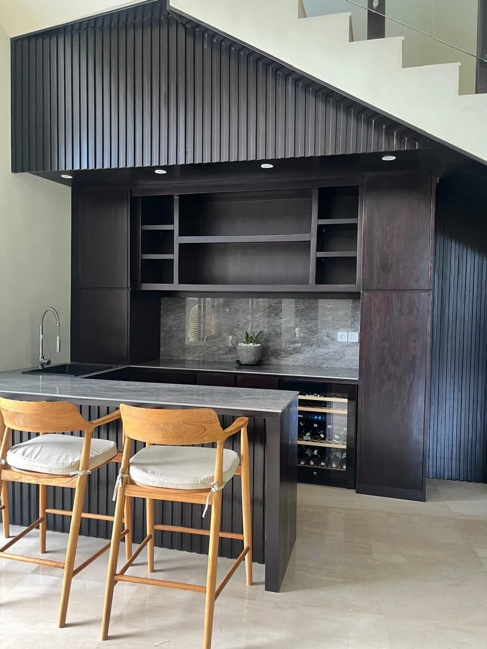 Fitted dark-stained timber joinery and a fluted bar counter built into an under-stair space