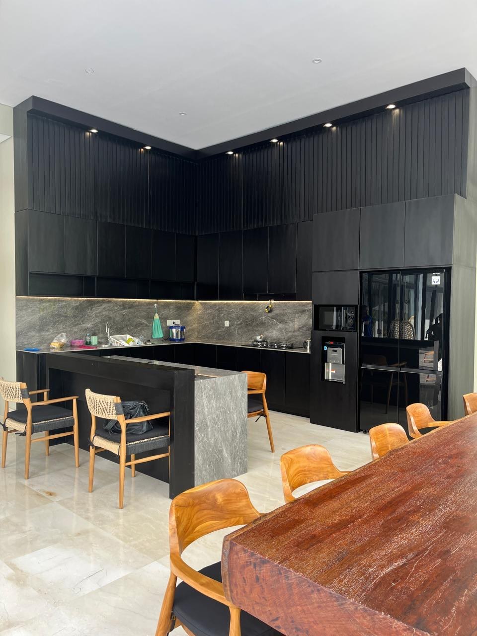 A black fluted-timber kitchen with stone counters and a live-edge suar dining table