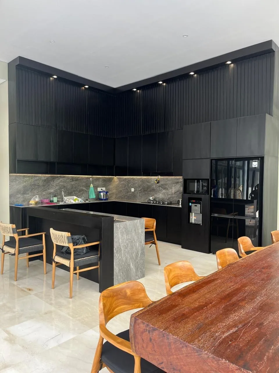 A black fluted-timber kitchen with stone counters and a live-edge suar dining table