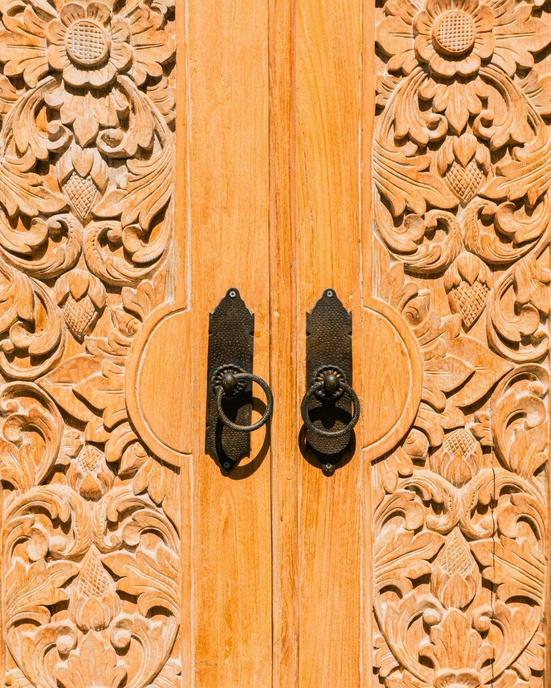 Close view of a hand-carved teak door with floral relief and cast-iron ring handles