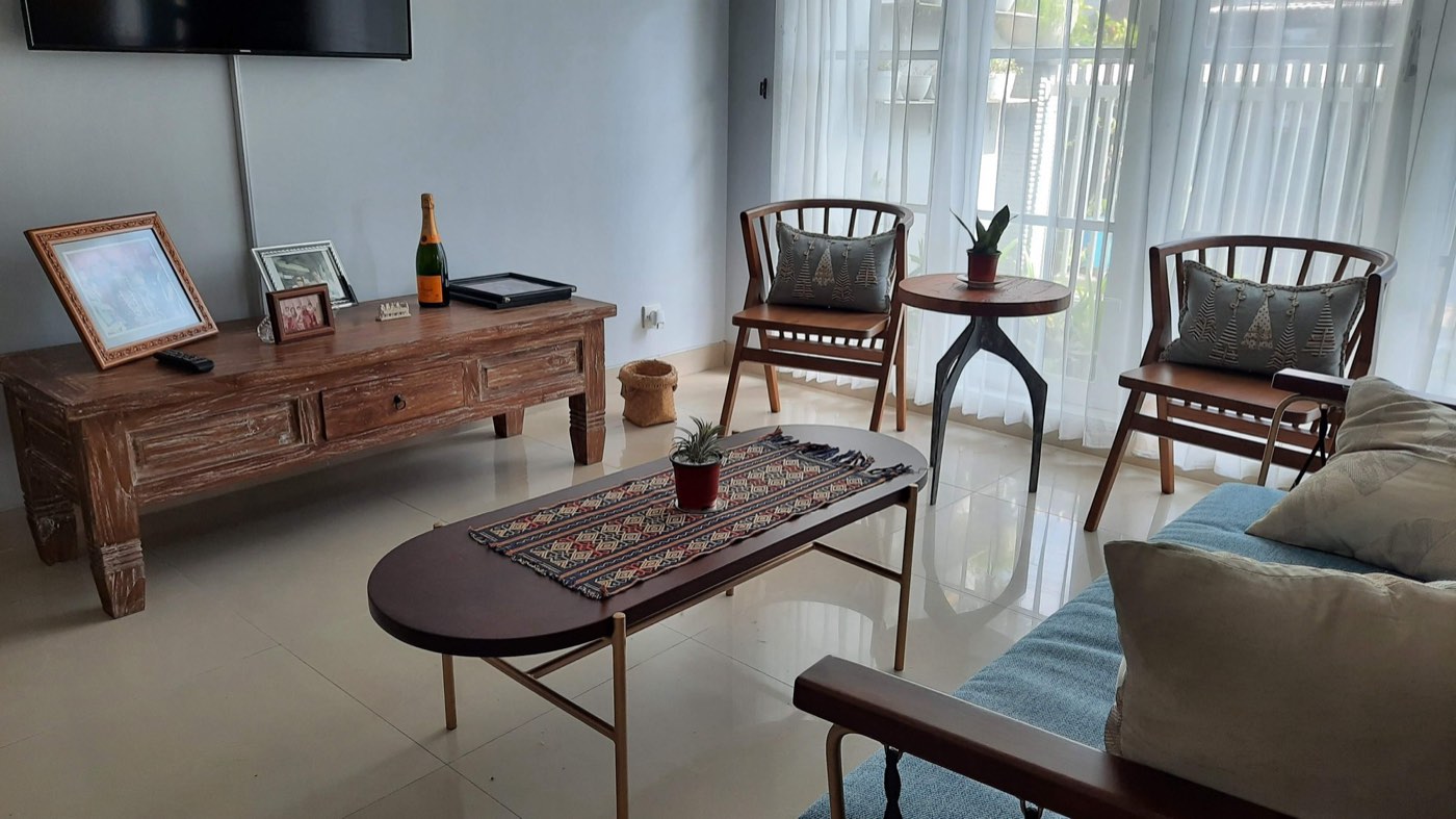 A villa living room furnished with a carved reclaimed-teak console, ikat textiles and slatted timber chairs