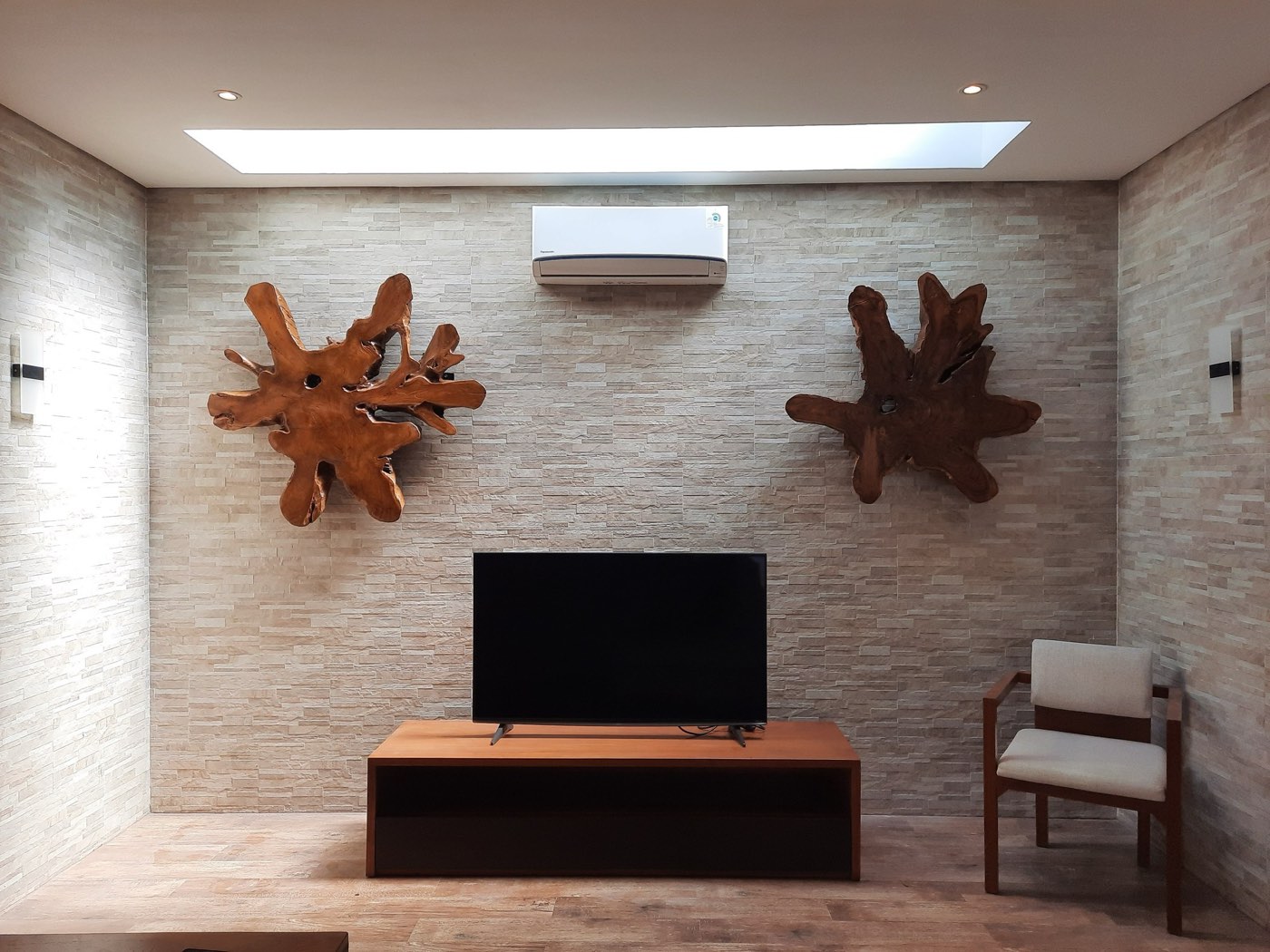 Two teak root-wood wall sculptures mounted on a stone wall above a timber console