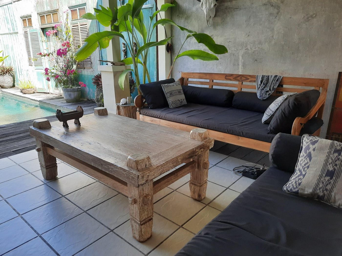 A poolside terrace with a reclaimed-teak daybed, low table and ikat cushions