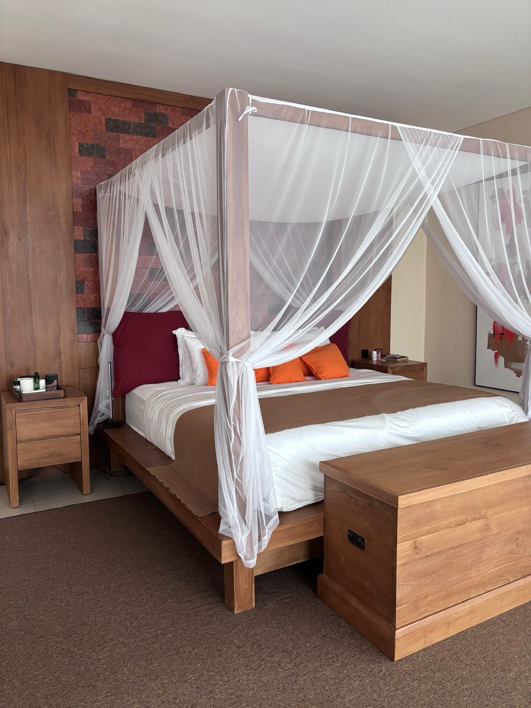 A solid teak four-poster bed with a white mosquito canopy, matching bedsides and a teak blanket chest