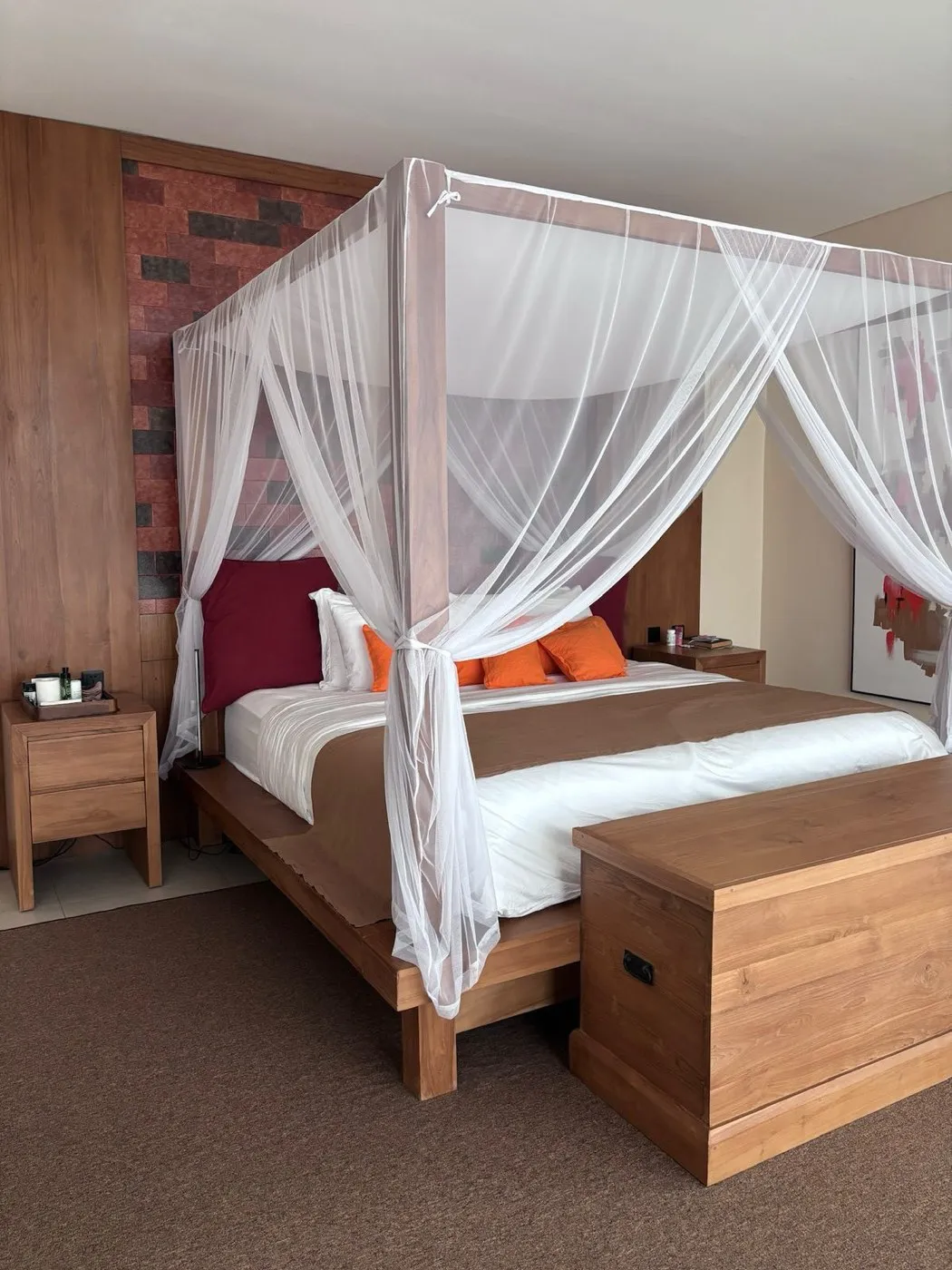 A solid teak four-poster bed with a white mosquito canopy, matching bedsides and a teak blanket chest