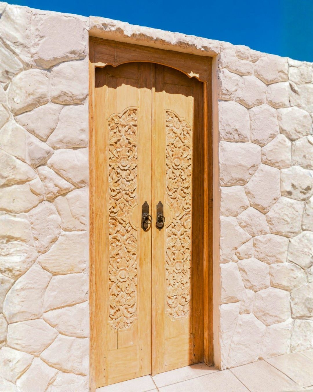 Hand-carved teak double door set into a white stone wall